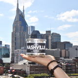 Hand holding the Nashville 100% soy wax candle in front of the downtown Nashville skyline