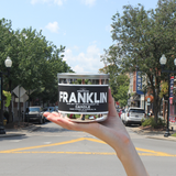 Hand holding the Franklin 100% soy wax candle on Main Street in downtown Franklin, Tennessee