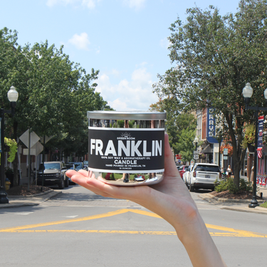 Hand holding the Franklin 100% soy wax candle on Main Street in downtown Franklin, Tennessee