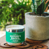 Spearmint & Basil candle on a wooden coaster beside a potted plant on a sunny patio