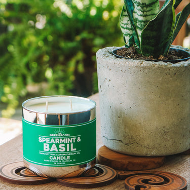 Spearmint & Basil candle on a wooden coaster beside a potted plant on a sunny patio