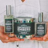 A woman in a white eyelet top holds three Green Mountain Candle products: a South Spray bottle, a Oakwood & Embers Candle tin, and a Preservative bottle.