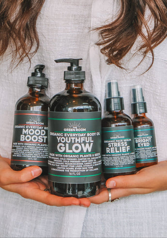 Four amber Green Room bottles held in two hands: Mood Boost and Youthful Glow organic body oils, Stress Relief face serum and Bright Eyed eye serum.