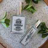 A bottle of GOLDEN HOUR spray cologne and a roller bottle sit on a white speckled background with greenery surrounding