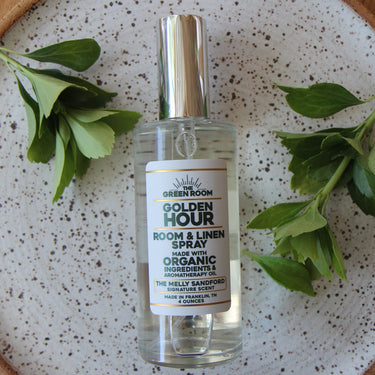 


A bottle of Golden Hour Room & Linen Spray by THE GREEN ROOM, styled on a speckled ceramic plate with green leaves and a slice of orange, set on a wooden tray.