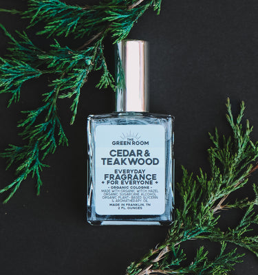 Cedar & Teakwood cologne with fresh cedar sprigs on a black background