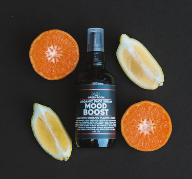 Mood Boost organic face serum with halved mandarins and lemon wedges on a black background