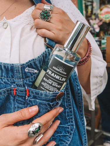 Person in overalls with a bottle of The Green Room Franklin organic room spray in their pocket.