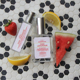 Pink Lemonade spray cologne and roll-on on black and white hexagon tile with watermelon and lemon