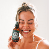 Woman holding a bottle of 'Youthful Glow' product with a plain background