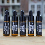 The Green Room 5 PC Face & Eye Serum Sampler Collection: five 5 ml amber dropper vials, Bright Eyed, Youthful Glow, Mood Boost, Stress Relief and Fragrance Free, lined up on a wood slab outside the shop on Main Street in Franklin, TN.